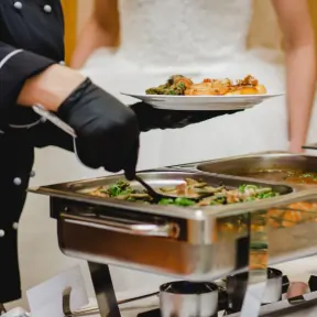 Caterer plating food from a buffet with the bride in lace visible behind